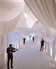 two men in suits playing violin under white draping with candles on the floor