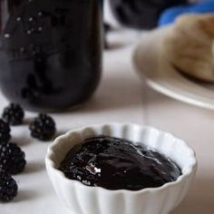 a bowl of blackberries next to a bottle of blackberry jam on a white table