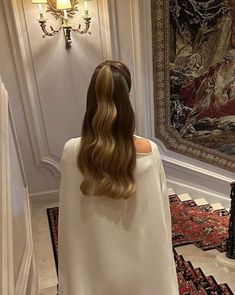 a woman with long hair standing in front of a wall hanging tapestry and looking at it