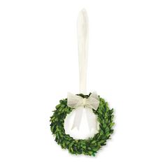 a green wreath with white bow hanging from the side on a white wall ornament