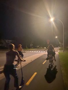 three people are riding their bikes down the street at night with one person on a scooter