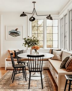 a dining room table with four chairs and a bench in front of the window,