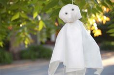 a white stuffed animal hanging from a string in front of some green leaves on a tree