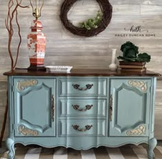 an old dresser painted in blue and gold with a wreath on the wall behind it