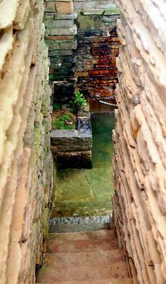 an alley way with stone walls and steps leading to a small pond in the middle