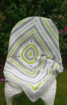 a white and green blanket sitting on top of a chair in the grass next to flowers