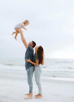 a man holding a baby up in the air while standing on top of a beach