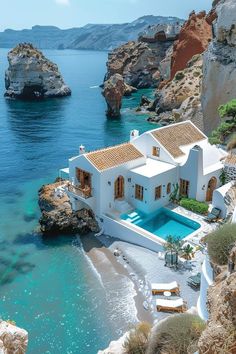 an aerial view of a white house on the beach with blue water and cliffs in the background