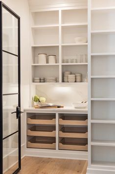 a kitchen with white shelves and wooden flooring next to an open door that leads to another room