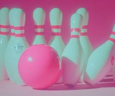 a pink and white bowling ball sitting next to some skittles on a pink background