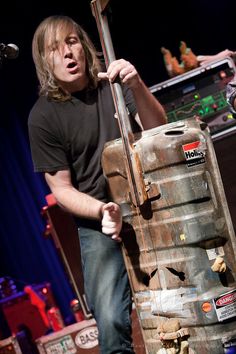 a man standing next to a wooden barrel holding a guitar in it's mouth