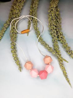 two necklaces are laying on top of some green plants and grass, one is pink