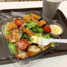 a plastic container filled with salad and dressing next to a cup of drink on top of a table