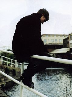 a man sitting on top of a rail next to a body of water