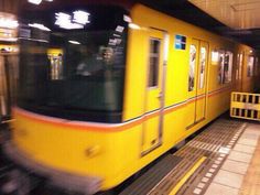 a yellow train traveling down tracks next to a loading platform