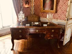 an antique desk in the corner of a room with ornate wallpaper and paintings on the walls