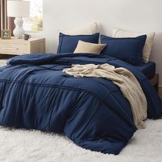 a bed with blue comforter and pillows on top of white fluffy carpeted floor