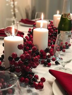 a table topped with candles and plates covered in red berries next to a bottle of wine