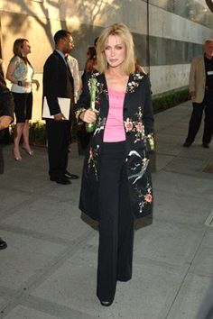 a woman in black pants and pink shirt walking down the street with other people behind her