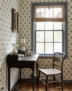 a desk and chair in front of a wallpapered room with a large window