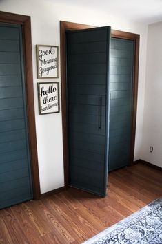 two black doors are open in the corner of a room with wood floors and white walls