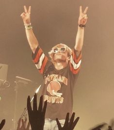 a man standing on top of a stage with his hands in the air and two fingers up