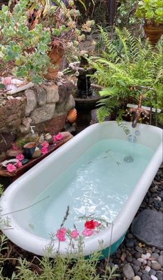 a bathtub filled with water surrounded by plants and rocks in a garden area next to a stone wall