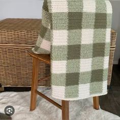 a green and white blanket sitting on top of a wooden chair next to a wicker basket