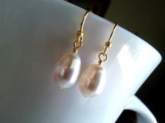 a pair of gold - plated earrings with white pearls are displayed on a coffee cup