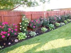 a garden filled with lots of flowers next to a wooden fence and green grass covered yard