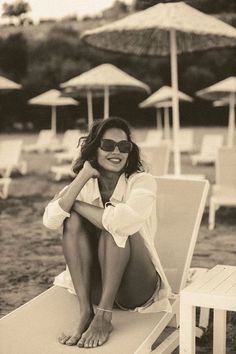 a woman sitting on top of a white chair next to umbrellas in the sand