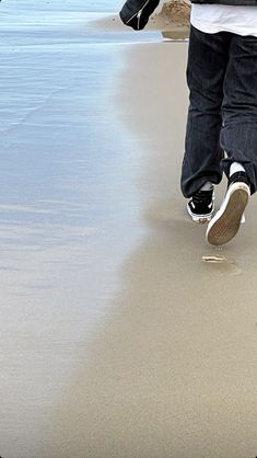 a person is walking on the beach with their feet in the sand and holding onto a skateboard