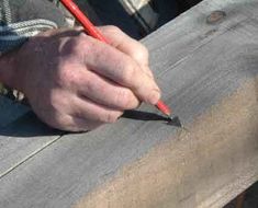 a person is holding a pencil and writing on a piece of wood that has been stained red