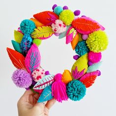 a person holding up a colorful wreath with pom - poms and leaves on it