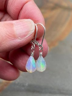 If you are into opals these earrings might be for you. White opal earrings in sterling silver. The minimalist earrings are handmade using white Ethiopian opals and sterling silver materials. A pair of opal stones (6.8 mm wide) with beautiful iridescent fire in mostly green and blue colors are used in the earrings. The earrings are mounted with simple leverback earring wires (shown). The stones are faceted and teardrop-shaped, one of the stones has a few tiny matrix dots. Opal is an October birthstone. The pair measures 1 1/4 inch (3.1 cm) long. These are the earrings you will receive.  Note: Ethiopian opals should be kept away from heat and water as this may alter their fire. The earrings ship in a small organza bag inside a gift box, ready to give... or keep! To see more WireAndPearl ster Hypoallergenic Opal Dangle Earrings, Hypoallergenic Sterling Silver Iridescent Jewelry, Hypoallergenic Iridescent Sterling Silver Jewelry, Adjustable Nickel-free Opal Earrings, Dainty Hypoallergenic Opal Earrings, Hypoallergenic Opal Drop Earrings, Minimalist Hypoallergenic Opal Earrings, Hypoallergenic Opal Dangle Jewelry, Opal Teardrop Earrings As Gift