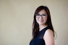 a woman wearing glasses standing in front of a beige wall with her arms crossed and smiling at the camera