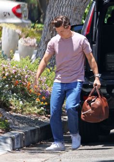 a man carrying a brown bag walking down the street next to a car and flowers