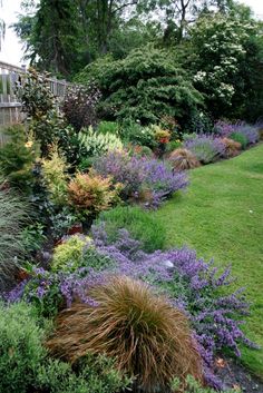 a garden filled with lots of different types of flowers and plants next to a wooden fence