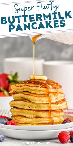 a stack of buttermilk pancakes on a plate with berries and syrup being drizzled over them