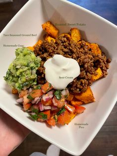 a hand holding a white square plate filled with taco salad and sweet potato wedges