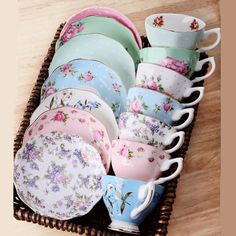 a basket filled with lots of colorful cups and saucers on top of a wooden table