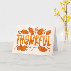 a card with the words, thank you in orange and yellow leaves on it next to a vase filled with flowers