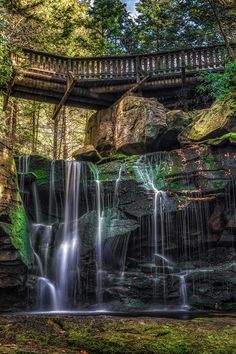 a waterfall in the woods with a bridge above it