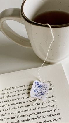 a cup of tea next to an open book with a piece of paper on it