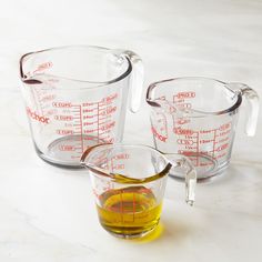 three measuring cups filled with liquid on top of a white counter next to an orange measuring cup