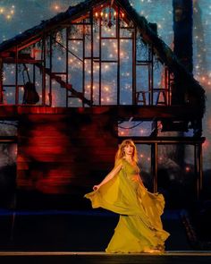 a woman in a yellow dress is on stage with lights behind her and a house