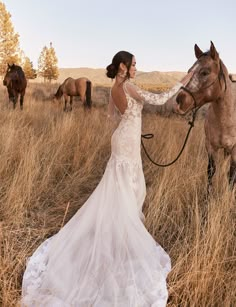 a woman in a wedding dress standing next to a horse on a dry grass field