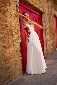 a woman in a white dress leaning against a red door