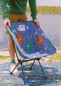 a man standing next to a blue lawn chair on top of a blanket covered ground