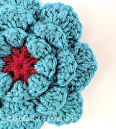 a crocheted blue flower with a red center on a white surface, close up